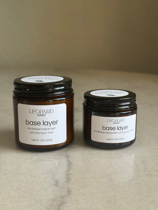 Two jars of Base Layer by Leopard Goods on a marble surface