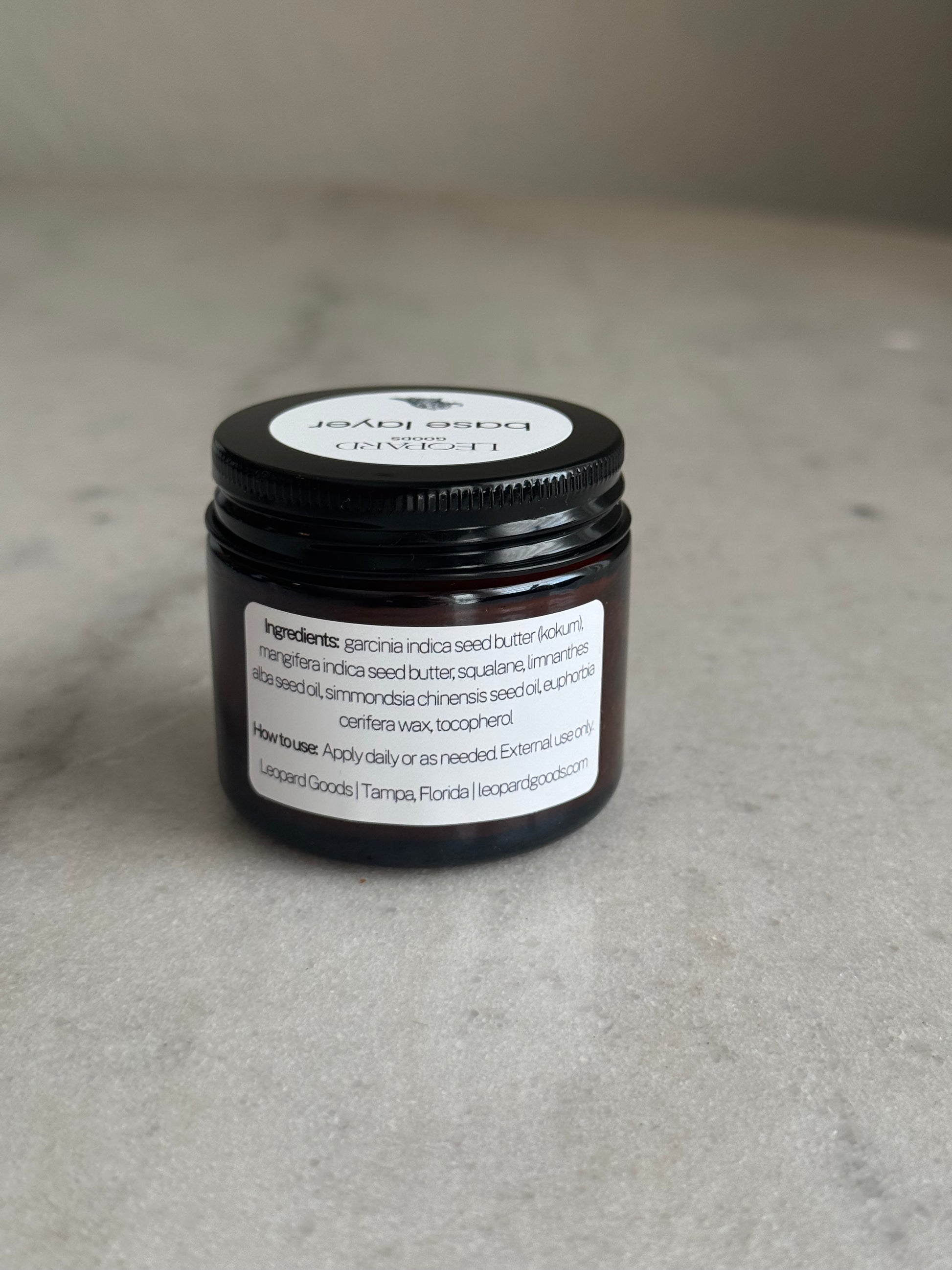 Back label of jar of Base Layer by Leopard Goods, 1.6oz, on a marble surface