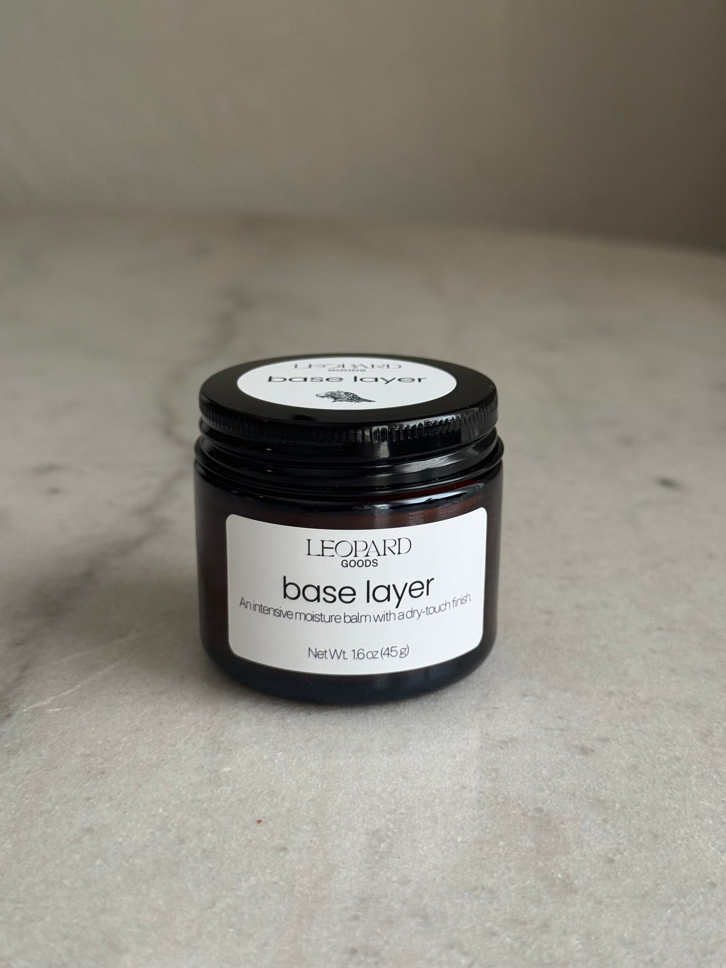 Front label of jar of Base Layer by Leopard Goods, 1.6oz, on a marble surface