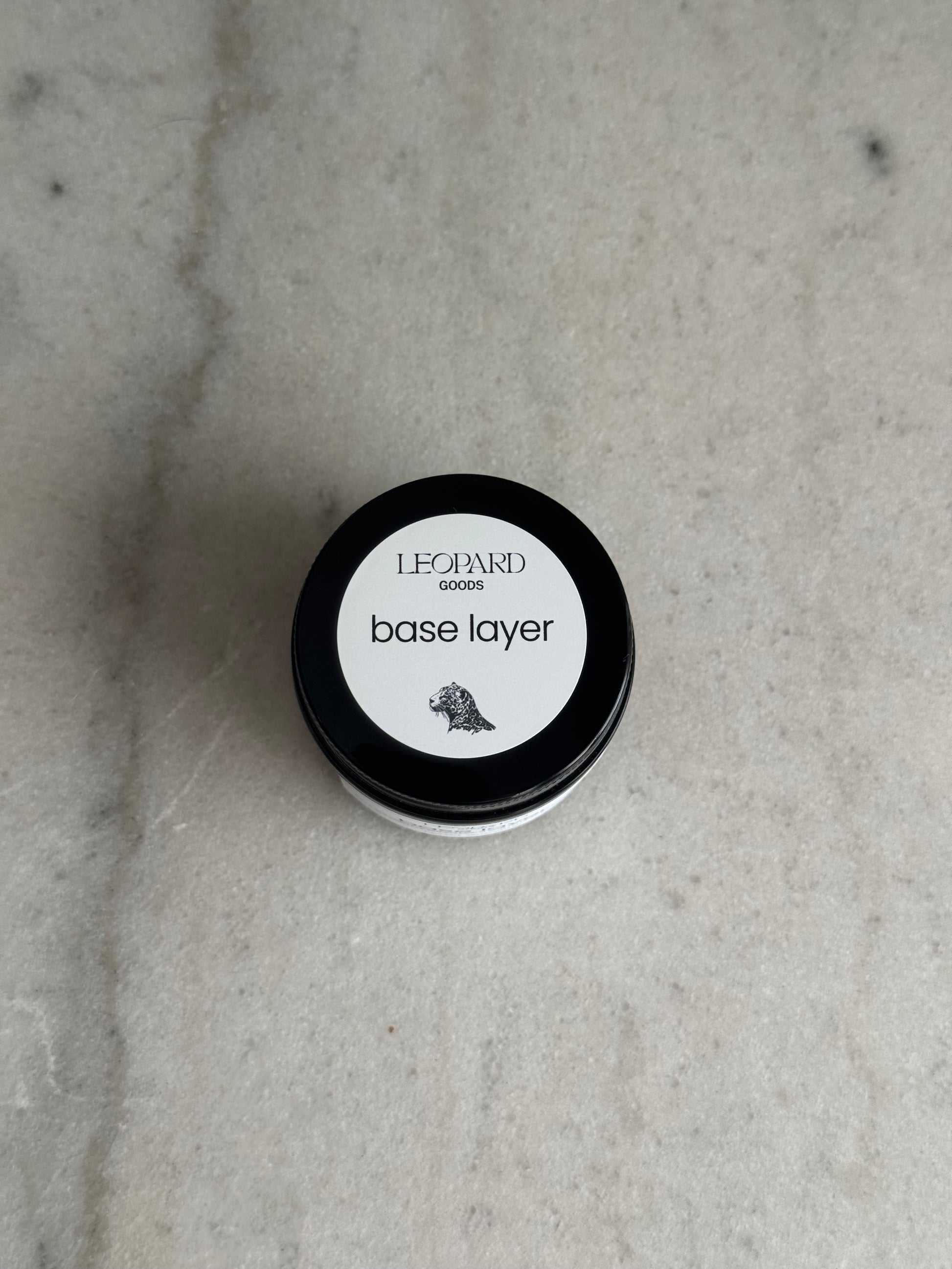 Top label of jar of Base Layer by Leopard Goods, 1.6oz, on a marble surface