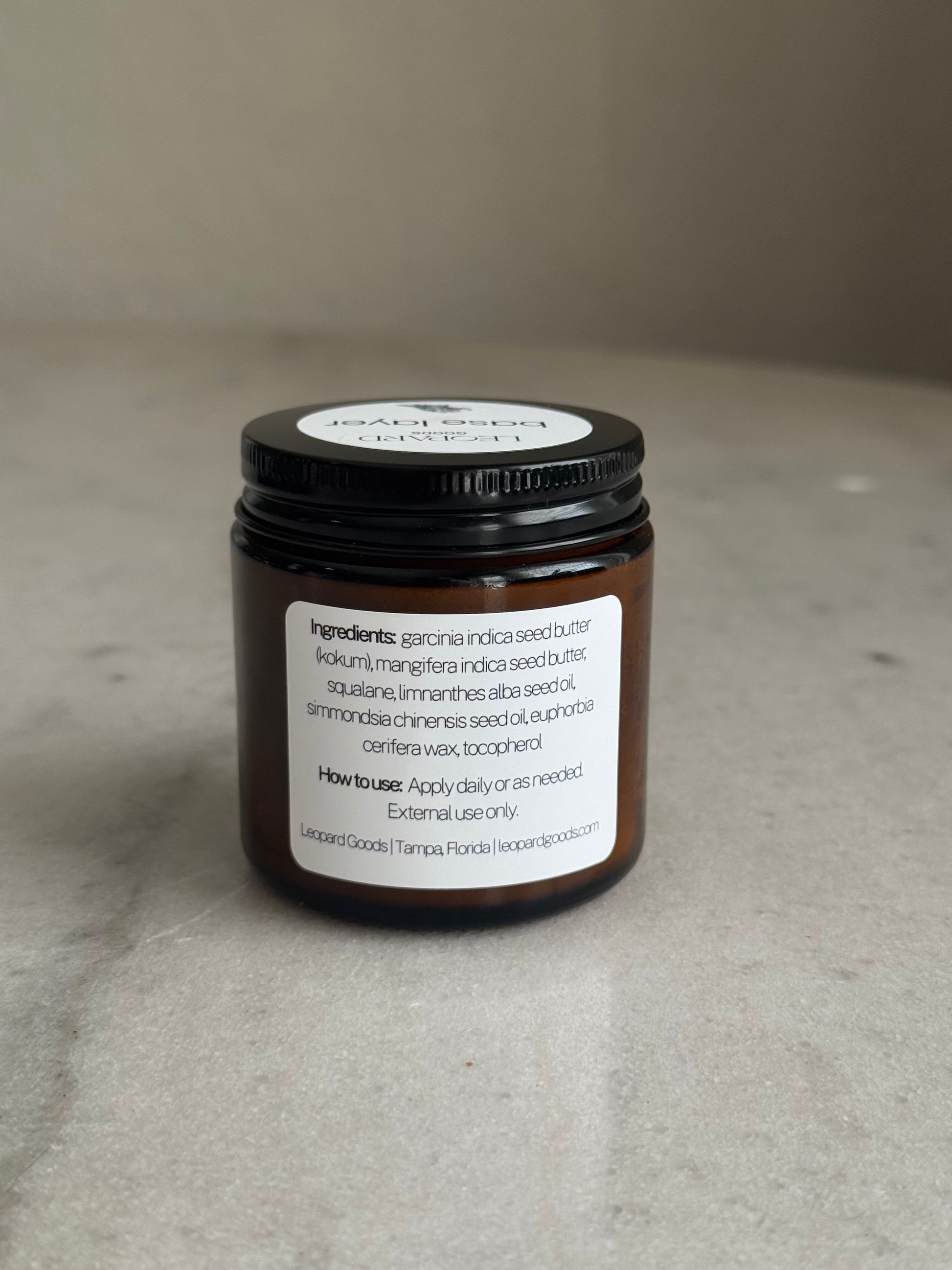 Back label of jar of Base Layer by Leopard Goods, 3.2oz, on a marble surface