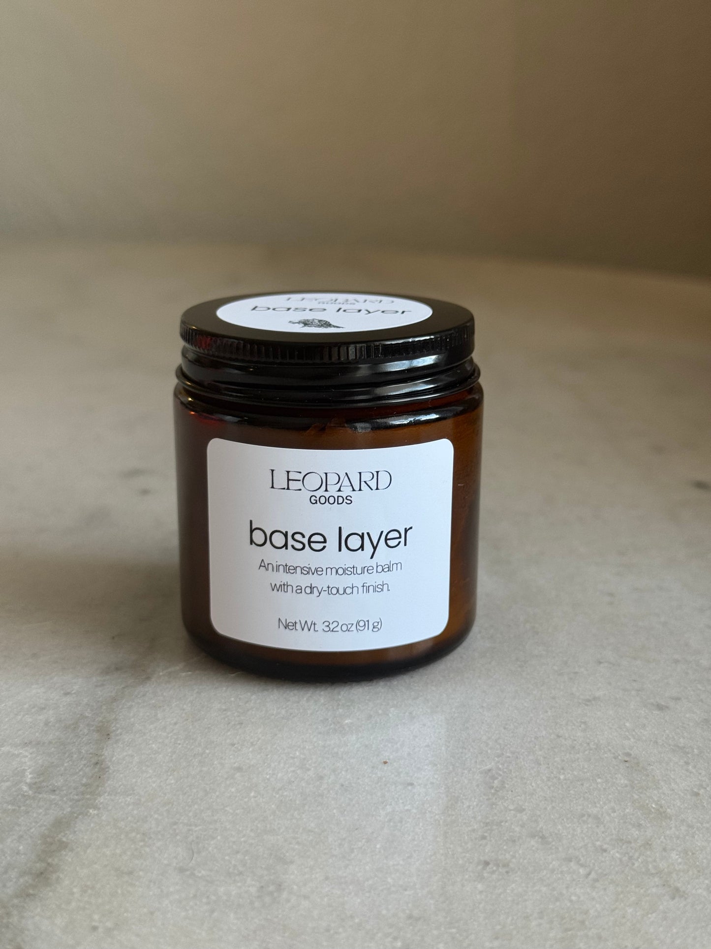 Front label of jar of Base Layer by Leopard Goods, 3.2oz, on a marble surface