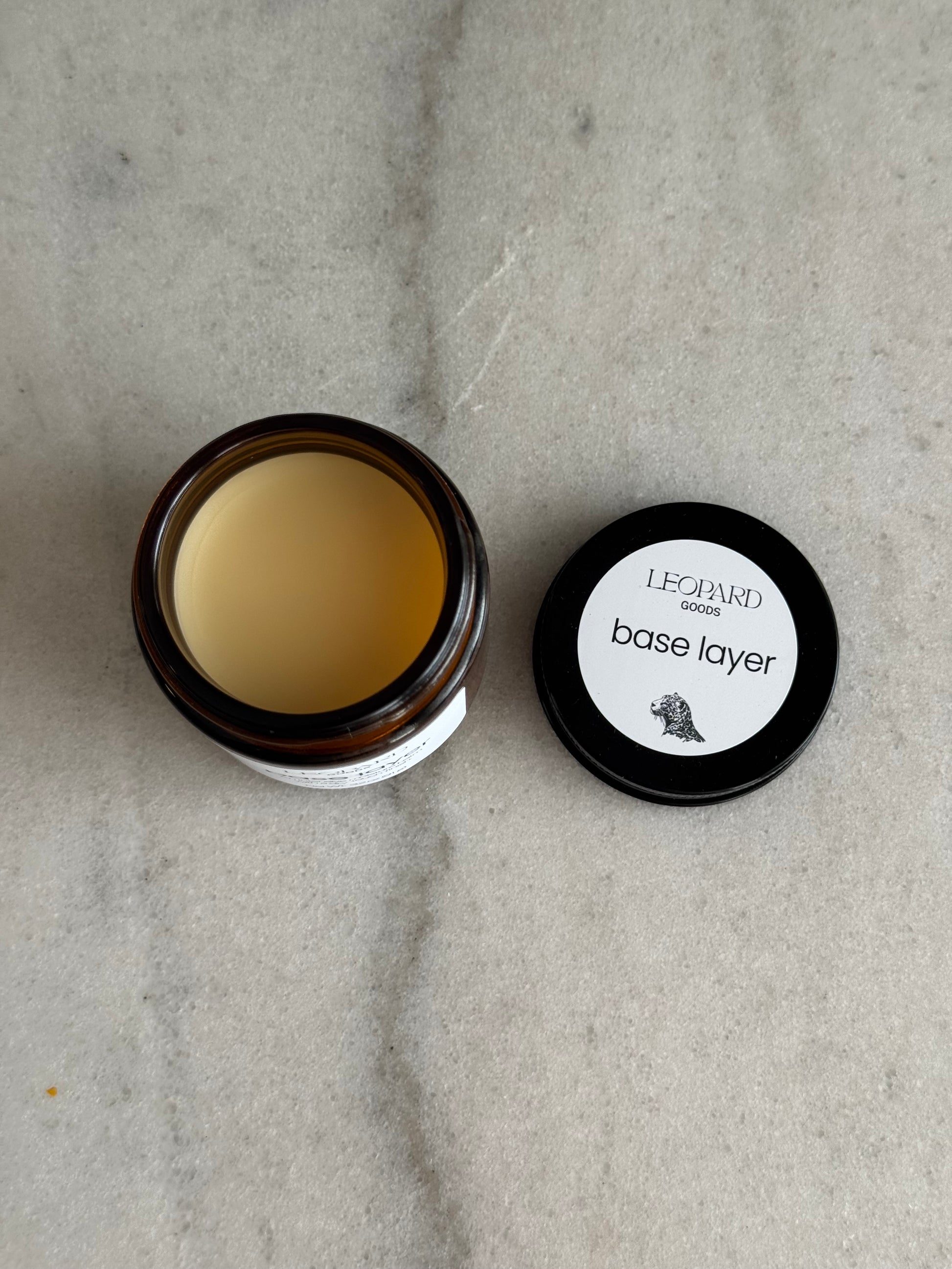 Open jar of Base Layer by Leopard Goods, 3.2oz, on a marble surface