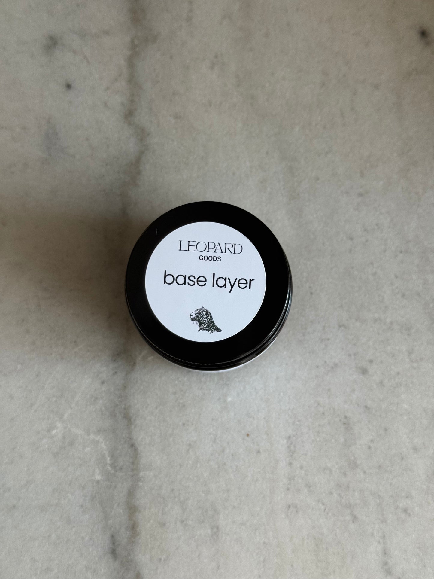 Top label of jar of Base Layer by Leopard Goods, 3.2oz, on a marble surface