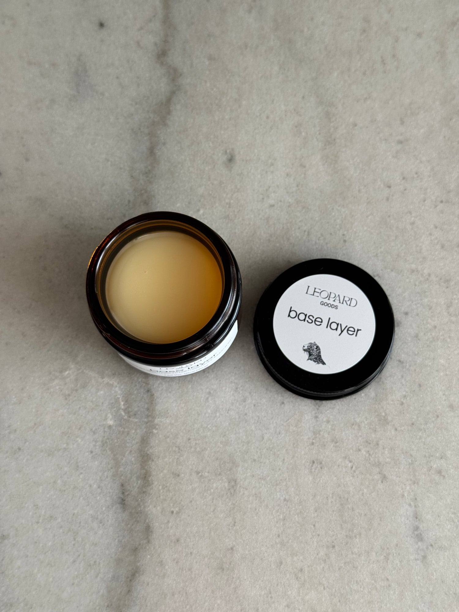 Open jar of Leopard Goods Base Layer on a gray marble surface
