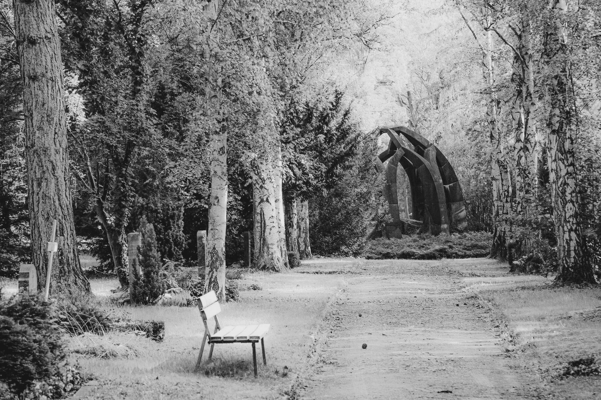 Monochrome image of a bench in a forest with a large stone sculpture in the background