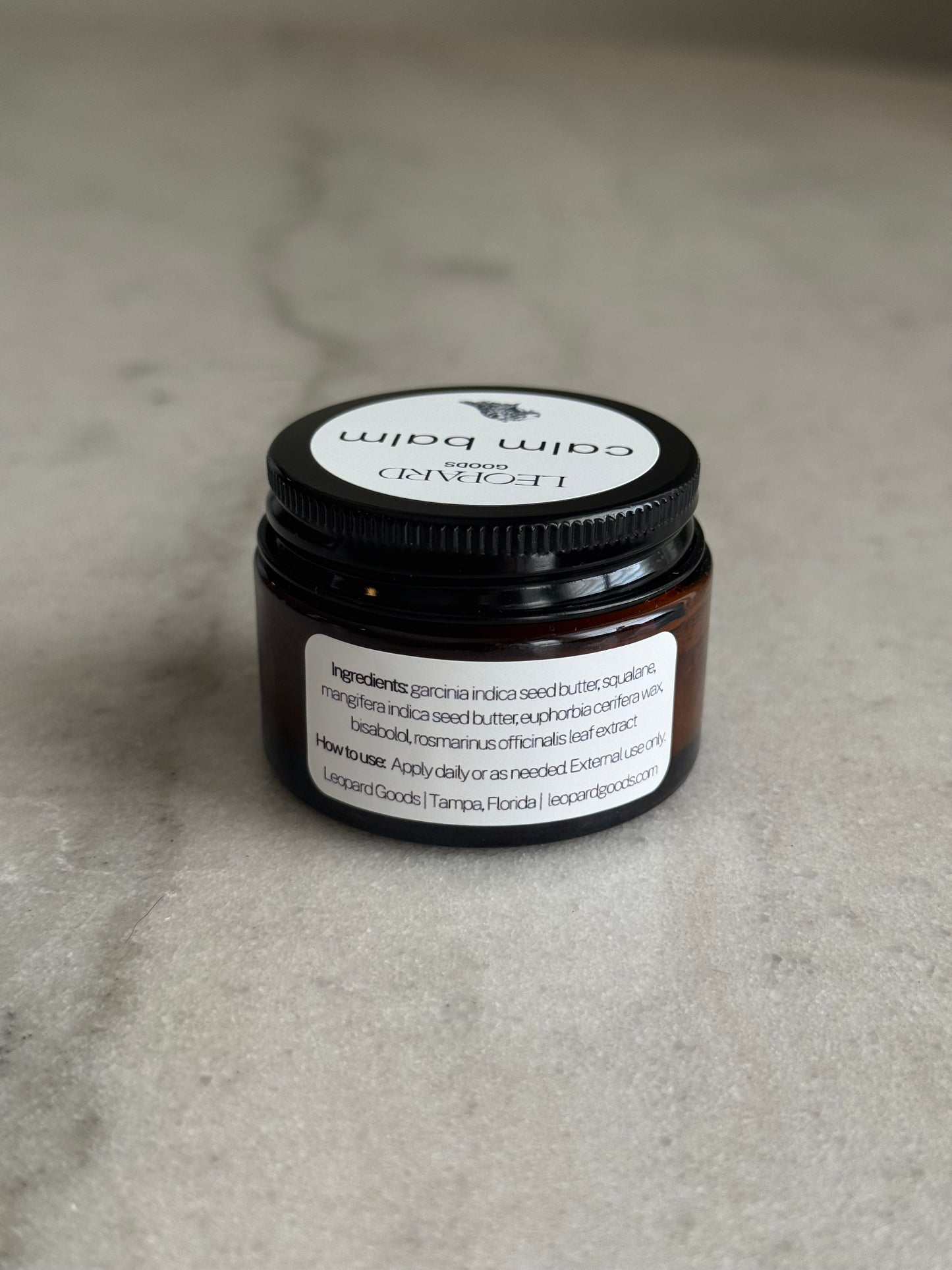 Back label of a 0.8oz jar of Calm Balm by Leopard Wellness on a marble surface