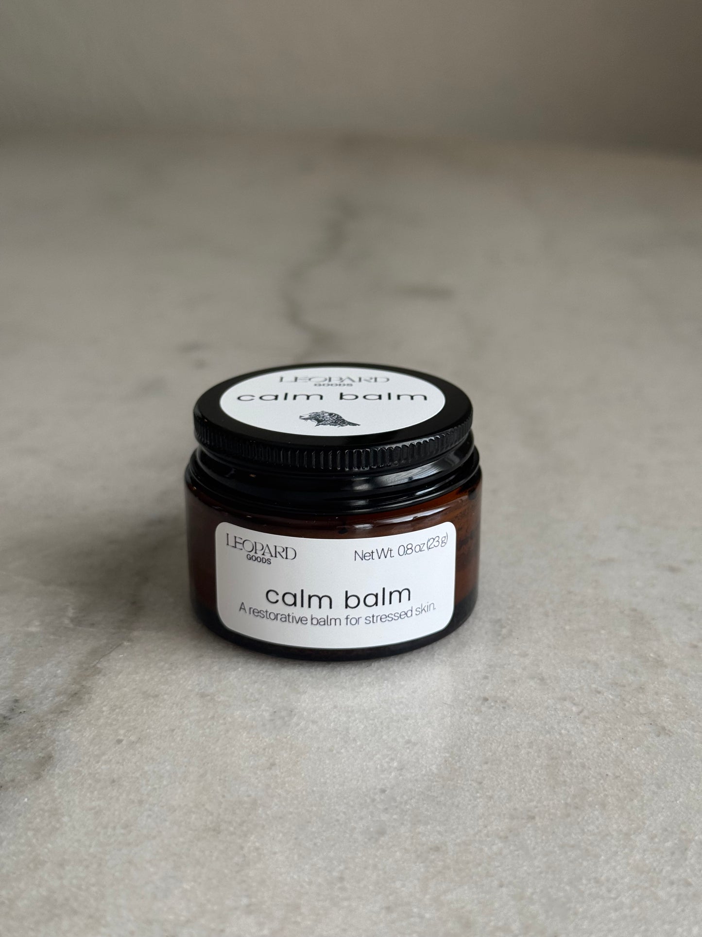 Front label of a 0.8oz jar of Calm Balm by Leopard Wellness on a marble surface