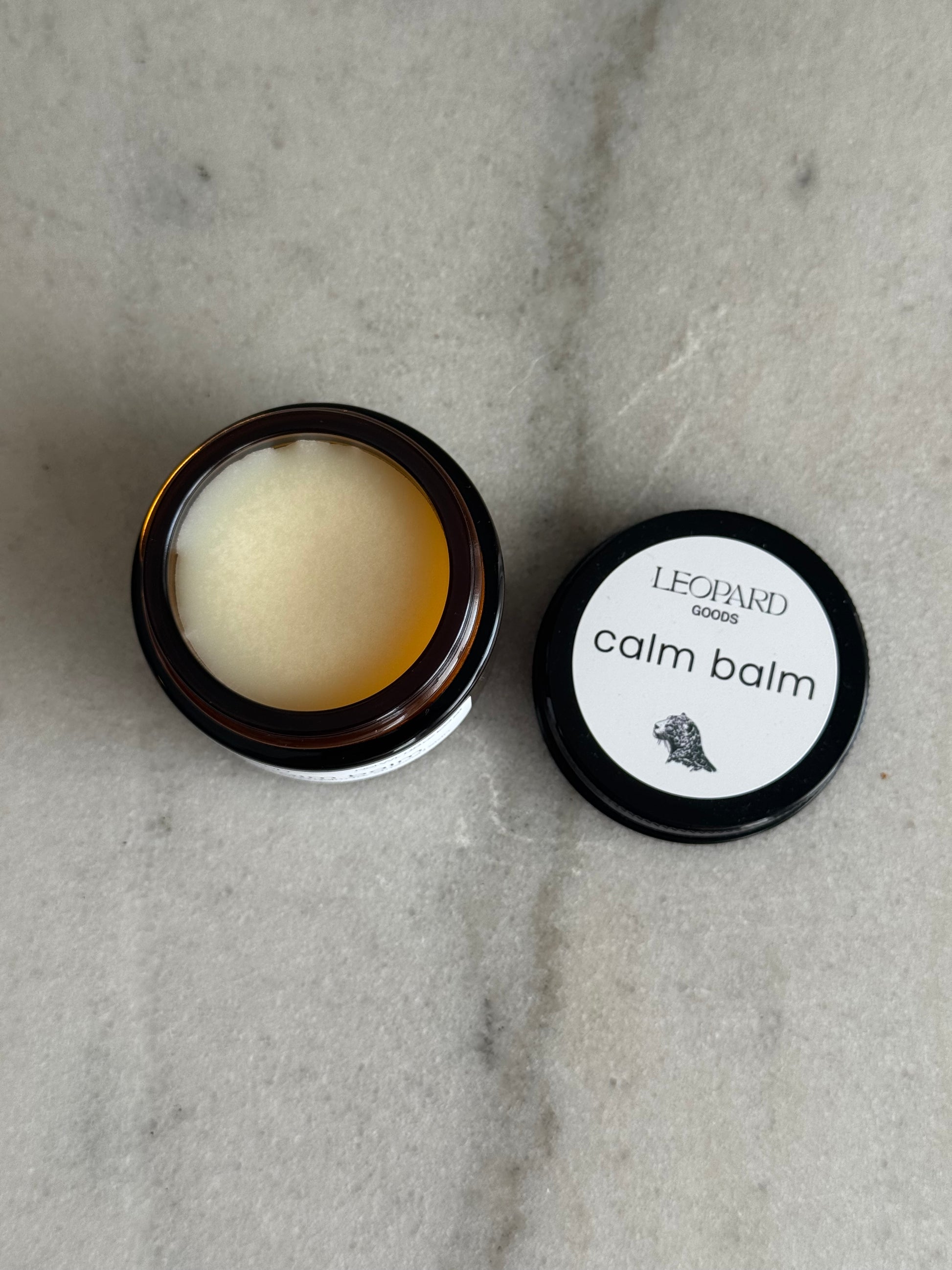 Open 0.8oz jar of Calm Balm by Leopard Wellness on a marble surface