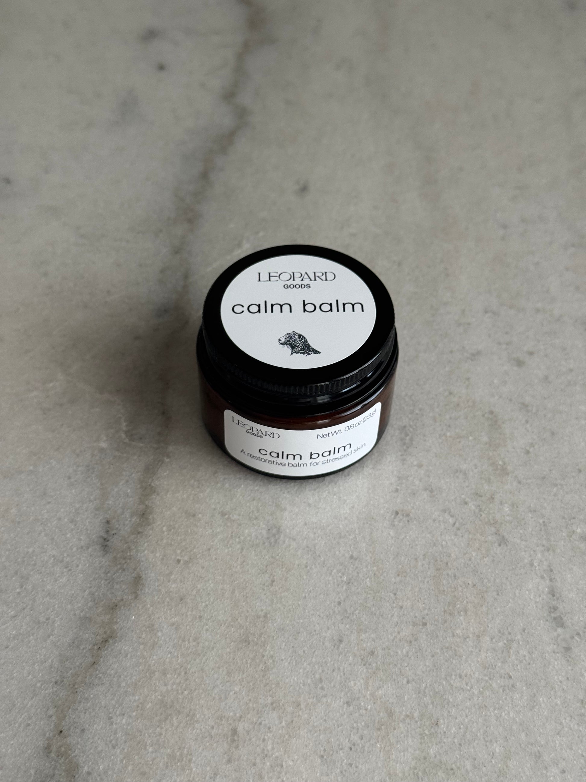 Overhead view of a 0.8oz jar of Calm Balm by Leopard Wellness on a marble surface