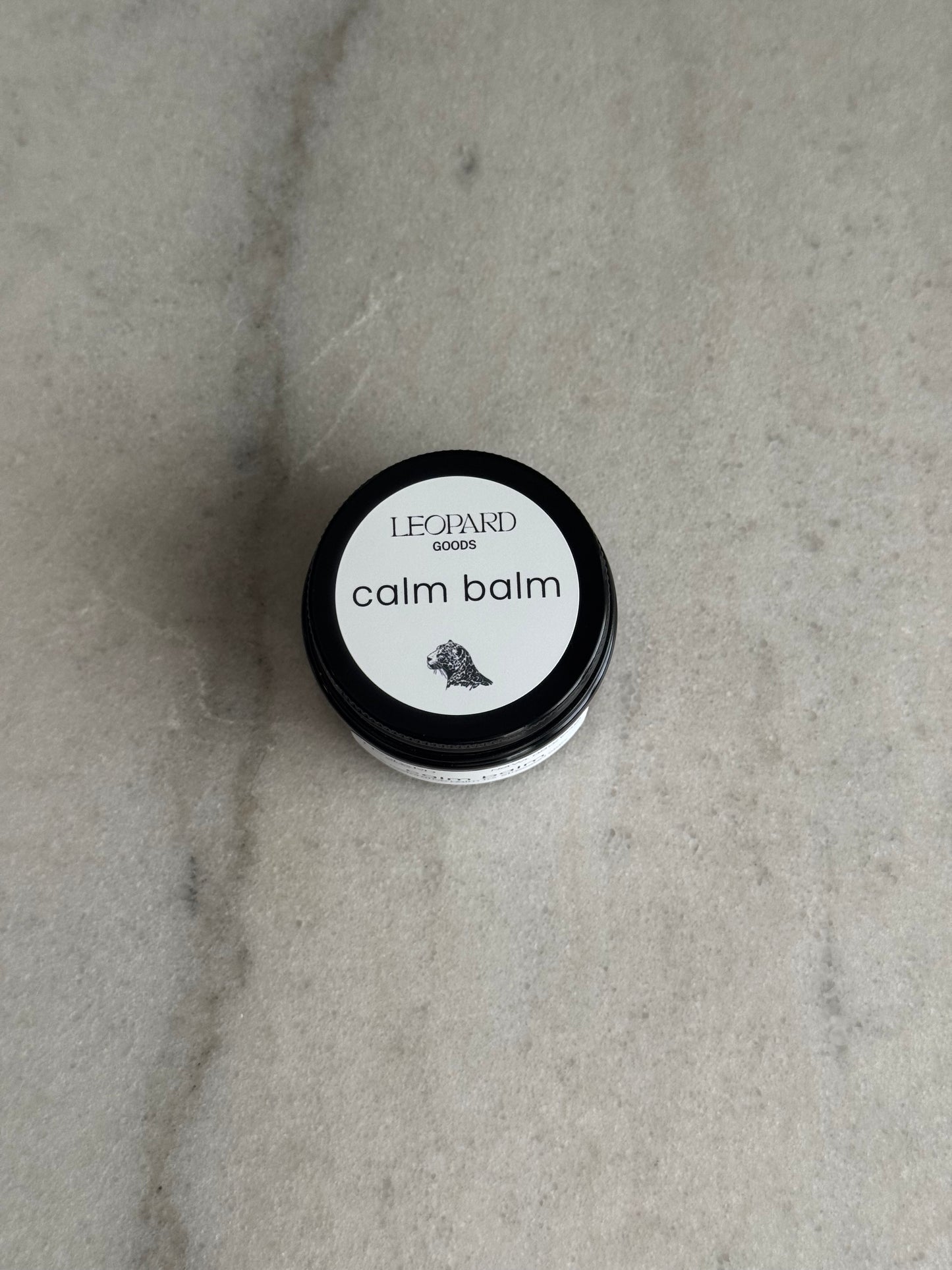 Top label of a 0.8oz jar of Calm Balm by Leopard Wellness on a marble surface
