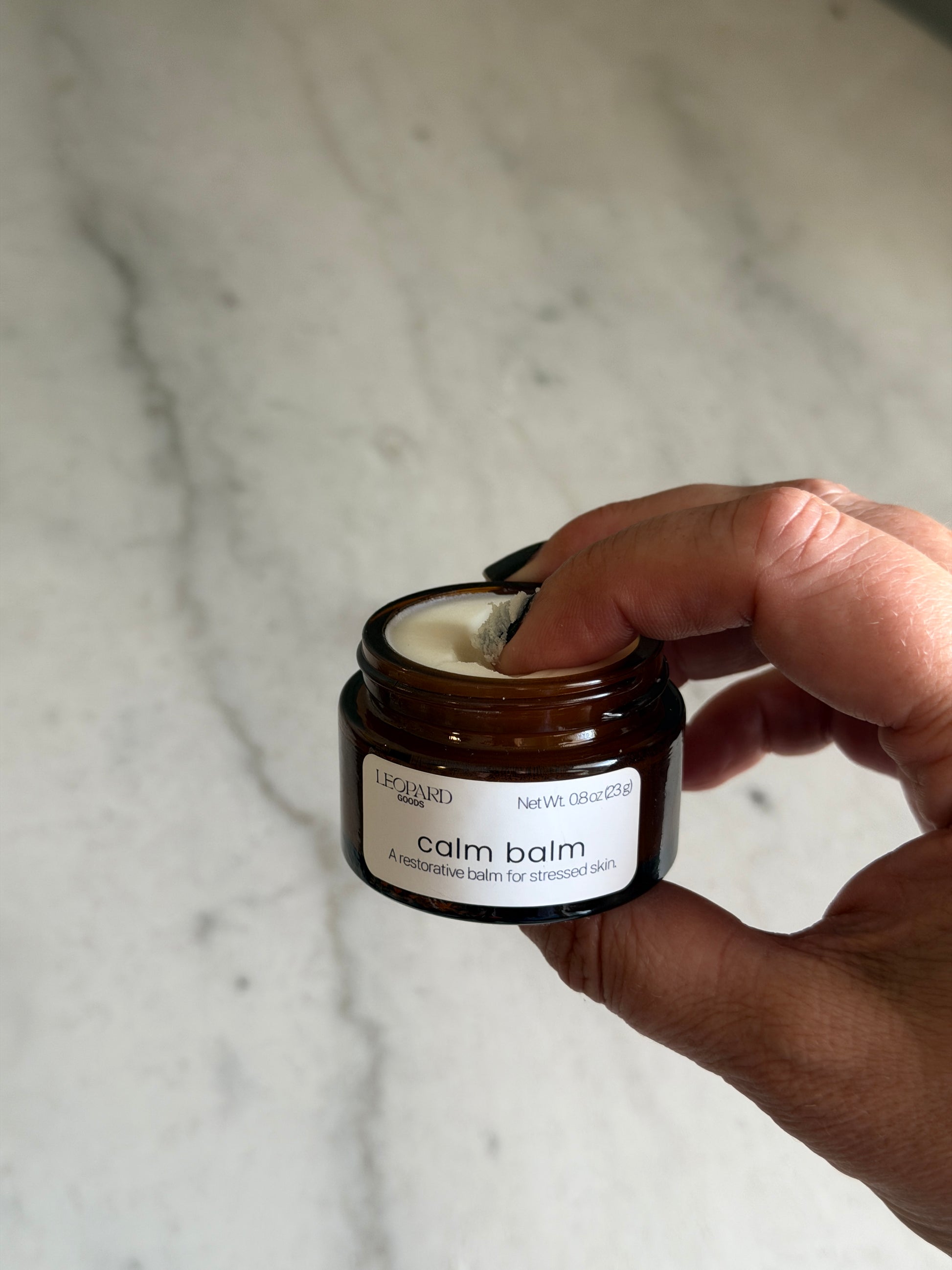 Hand holding a small jar of Calm Balm by Leopard Goods on a marble surface