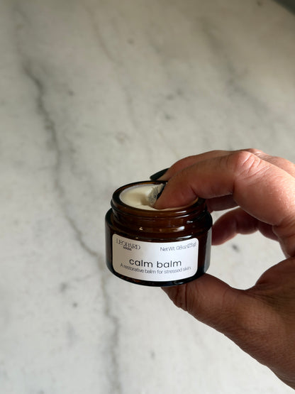 Hand holding a small jar of Calm Balm by Leopard Goods on a marble surface