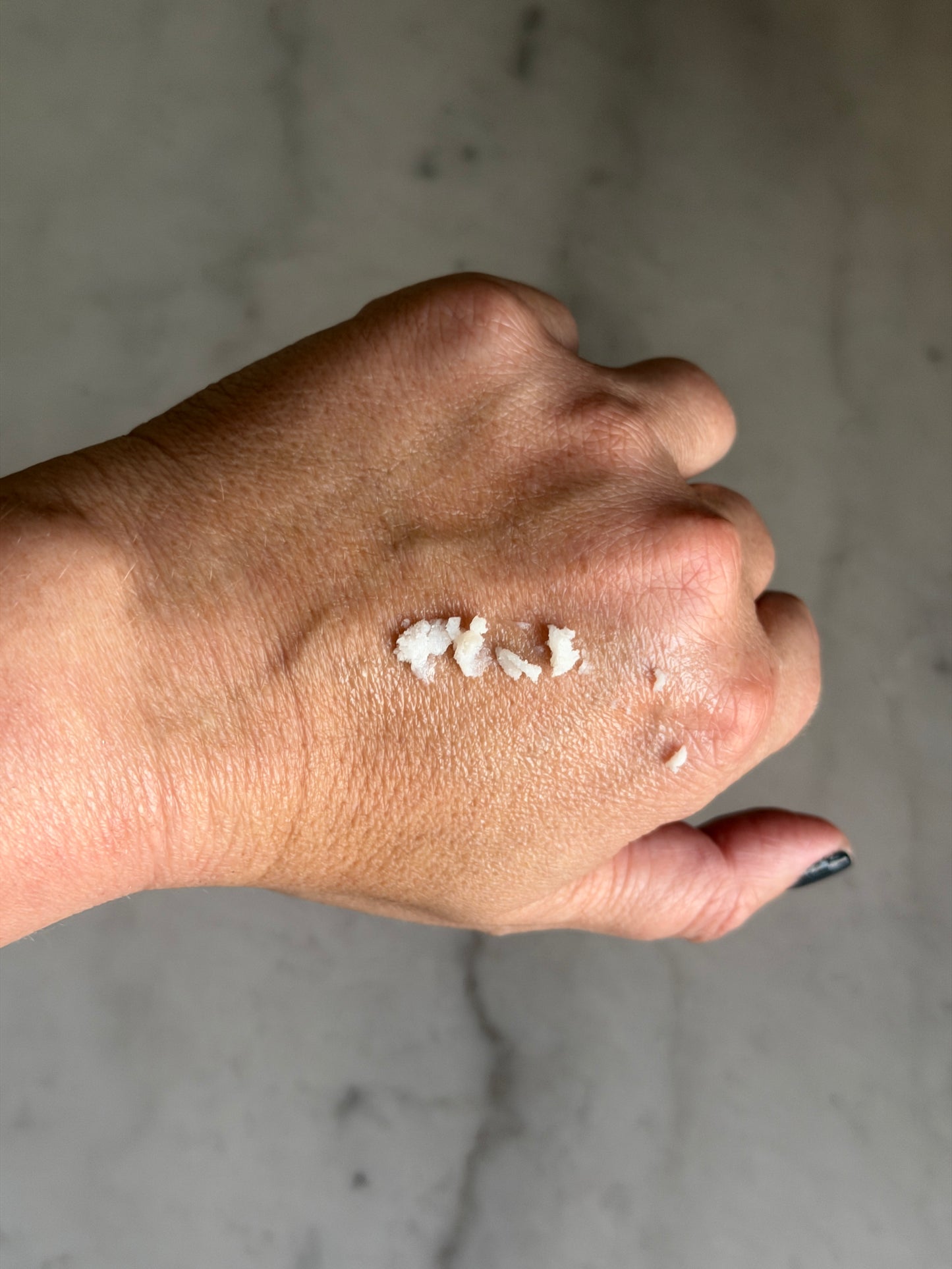 Hand with a small amount of Calm Balm by Leopard Goods on the back, not yet rubbed in, against a gray marble surface