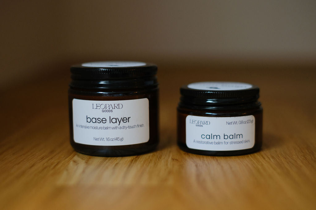 Two jars of balm, Base Layer and Calm Balm, on a wooden surface